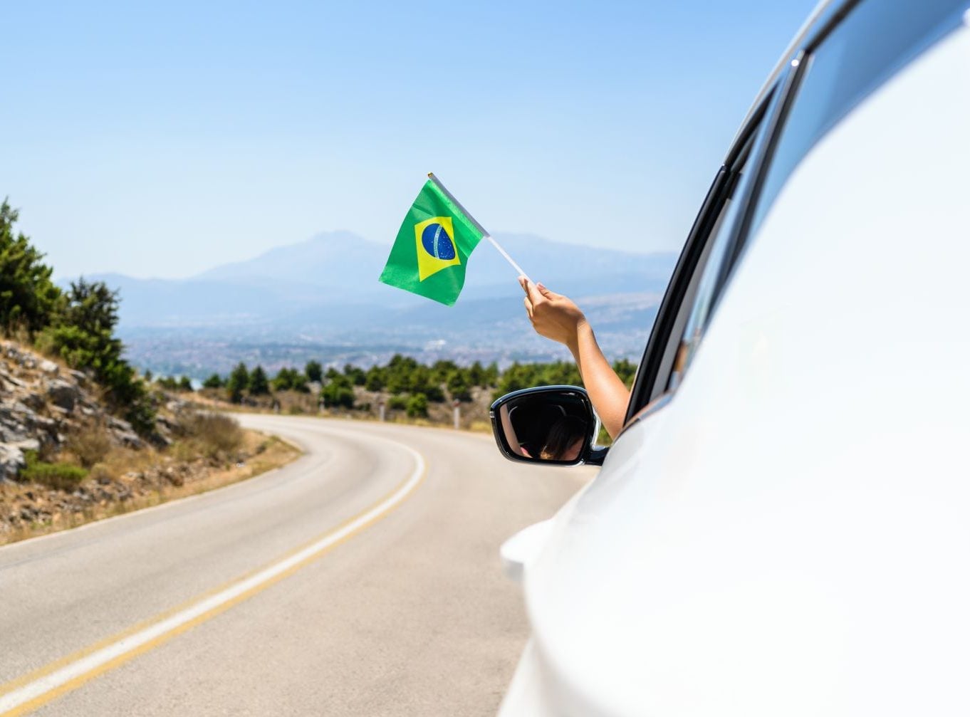 motorista segurando bandeirinha do brasil para fora da janela enquanto dirige shutterstock